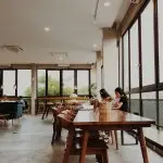 Digital nomads working at long wooden communal tables in a bright, open co-working space in Europe
