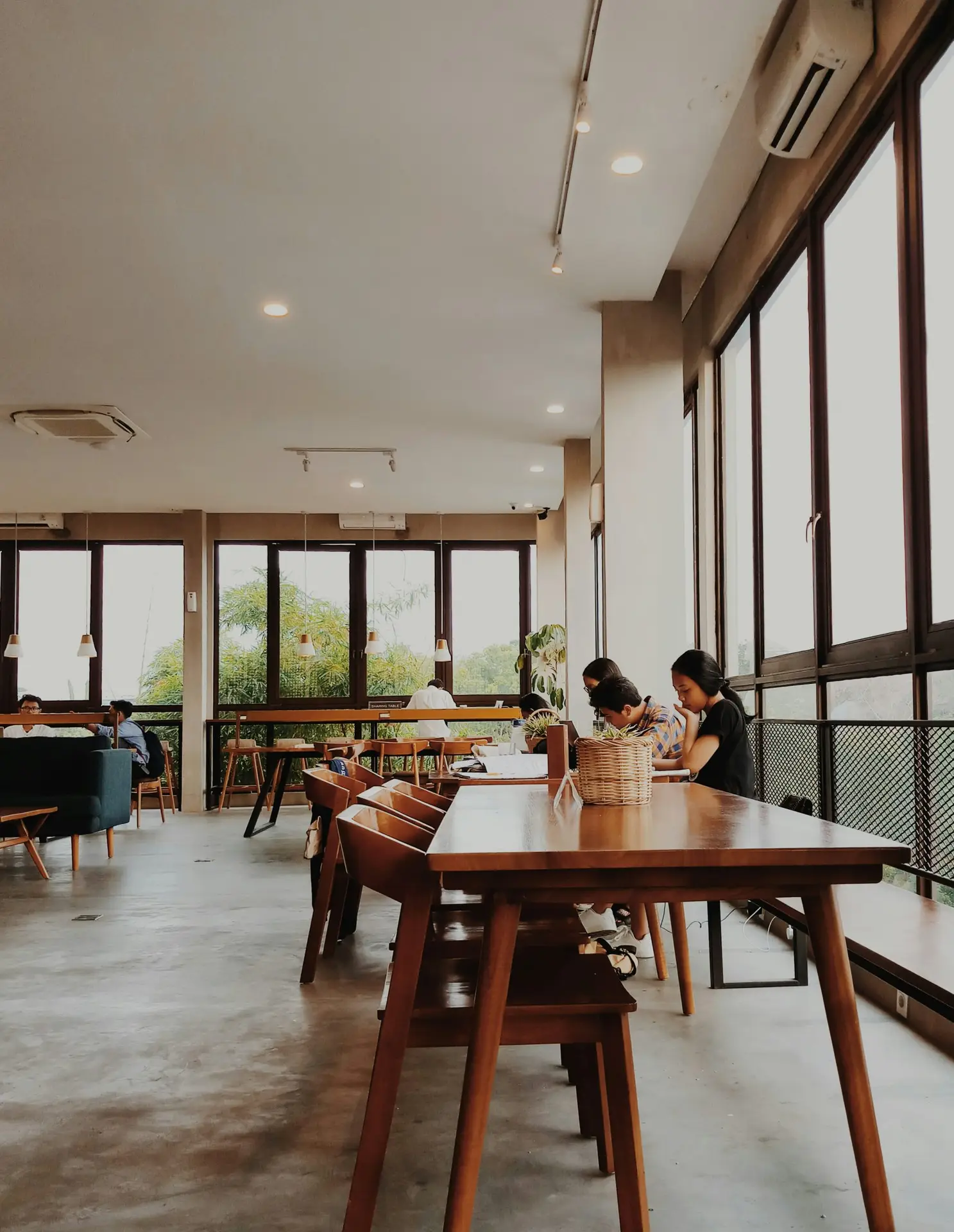 Digital nomads working at long wooden communal tables in a bright, open co-working space in Europe
