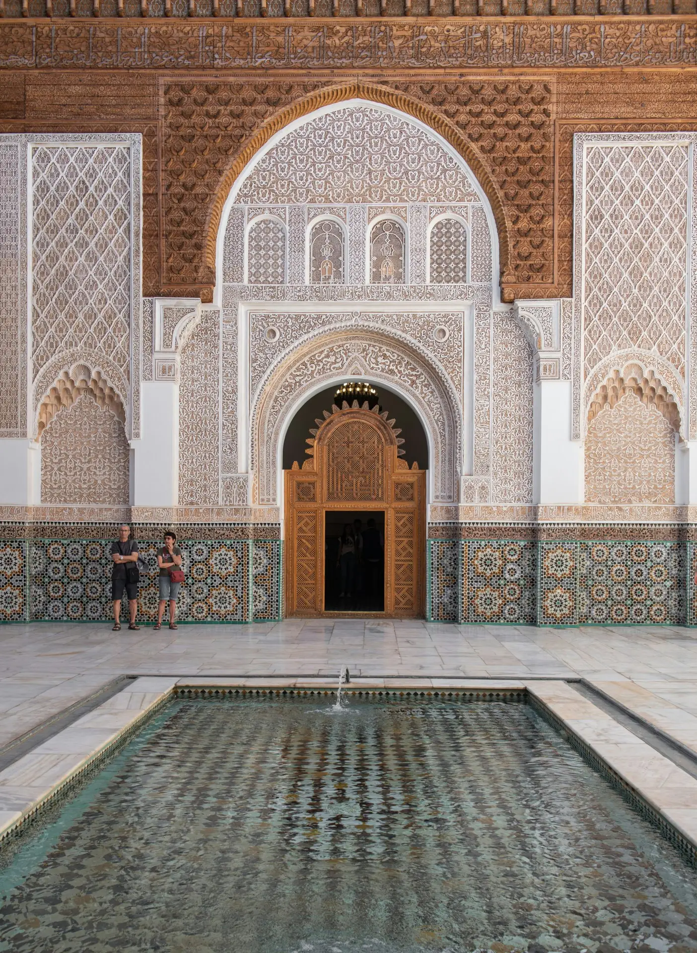 Ben Youssef Madrasa courtyard in Marrakech with mosaic tiles, carved stucco walls, and reflecting pool