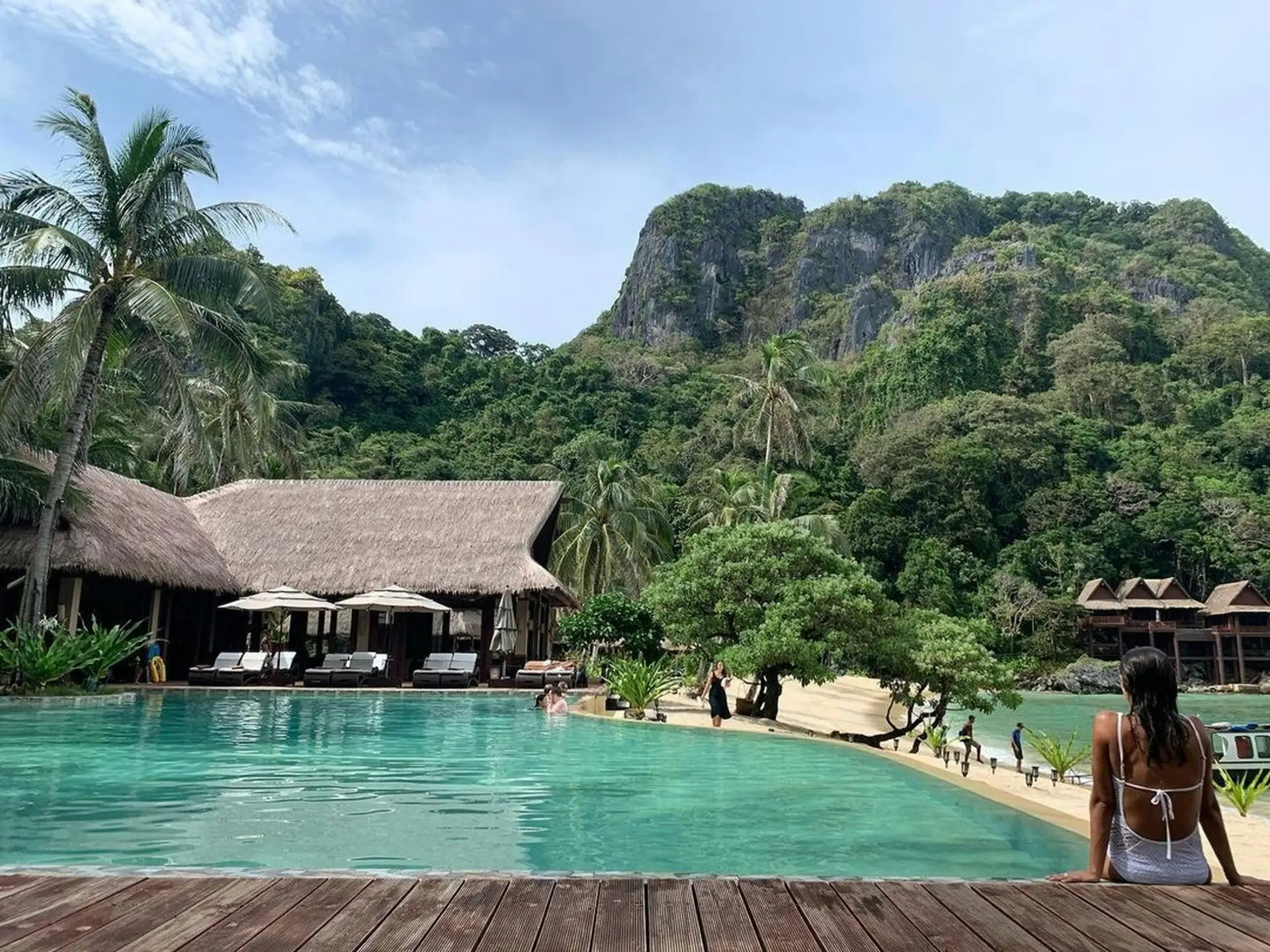 The infinity pool at Cauayan Boutique Private Island with the thatched Horizon Restaurant, white sand beach and Bacuit Bay limestone karsts behind