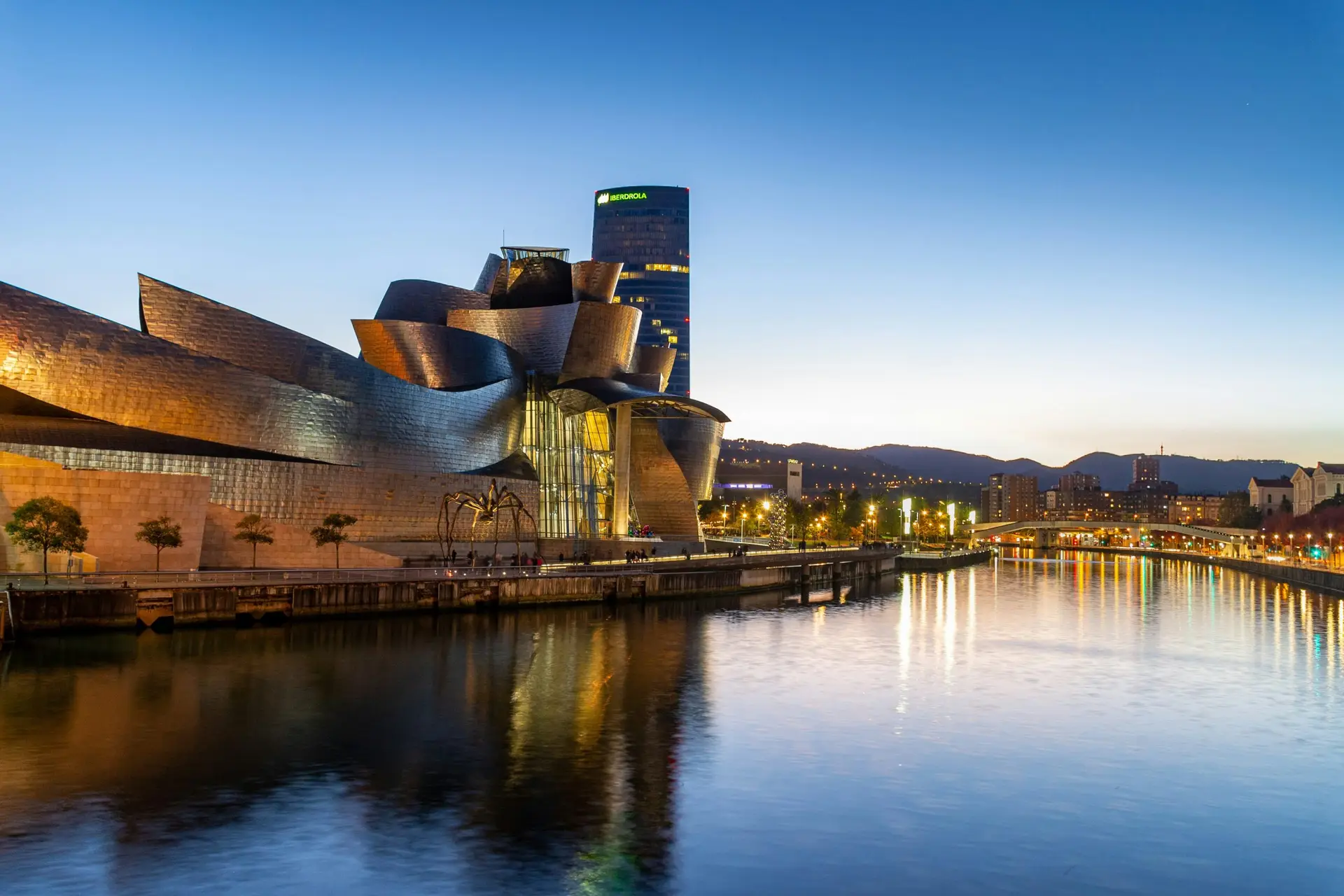 Guggenheim Museum Bilbao with its titanium facade reflected in the Nervión River at dusk, designed by Frank Gehry