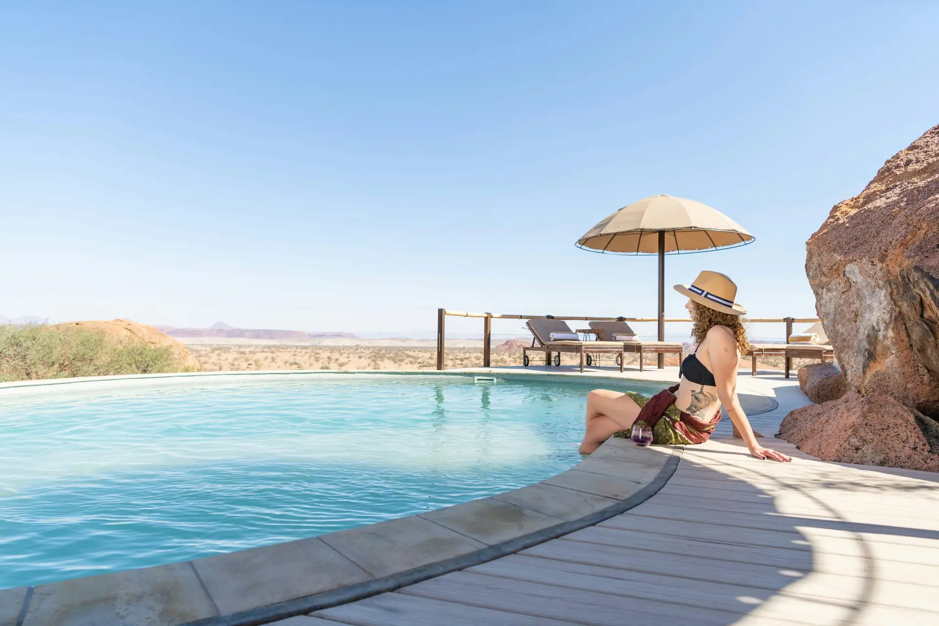 A guest relaxes by the pool at Onduli Ridge, built into the granite boulders with views across the Damaraland plains