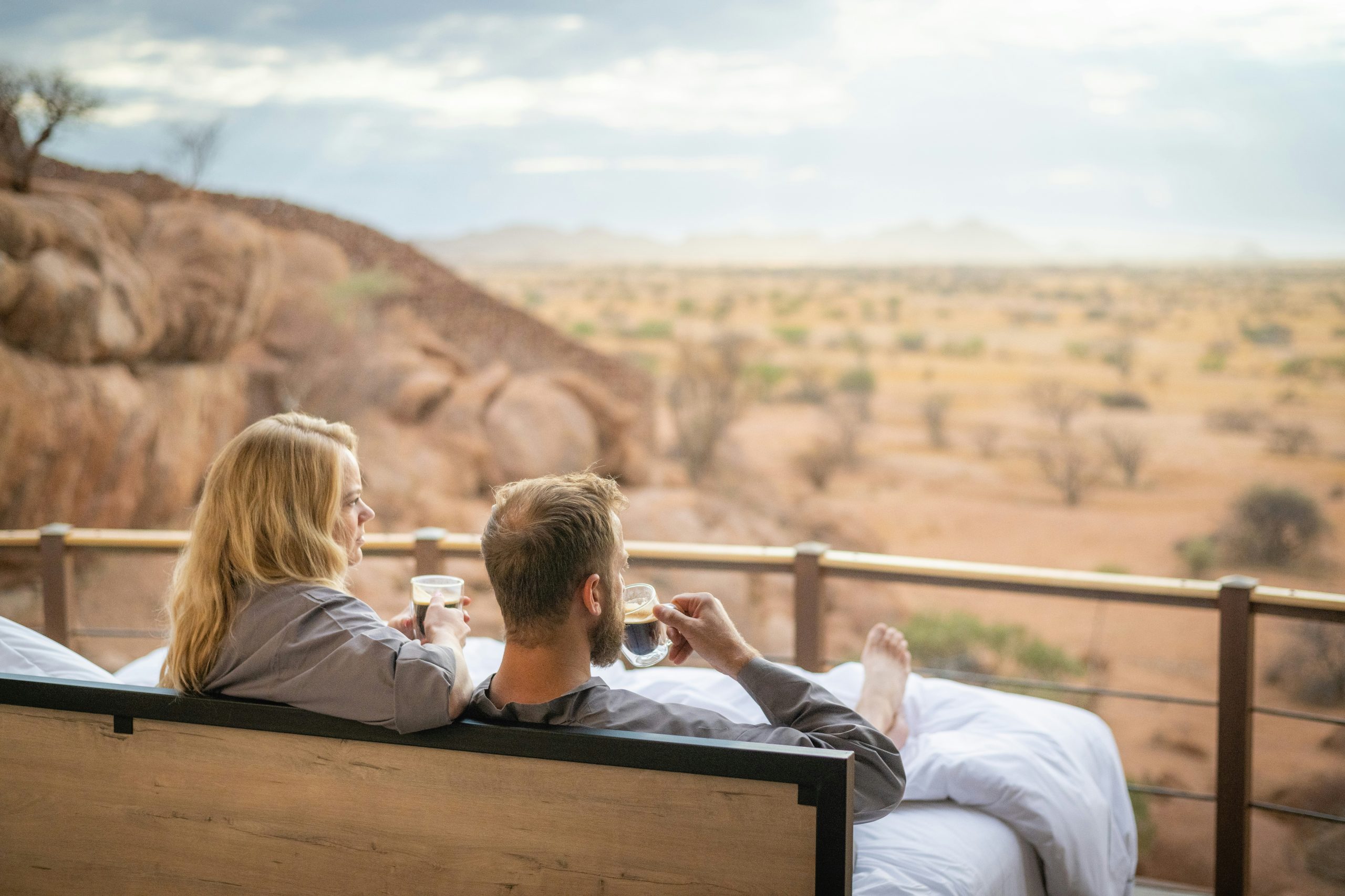  A couple in robes drinking coffee in the star bed on their private terrace at Onduli Ridge, overlooking the Damaraland landscape