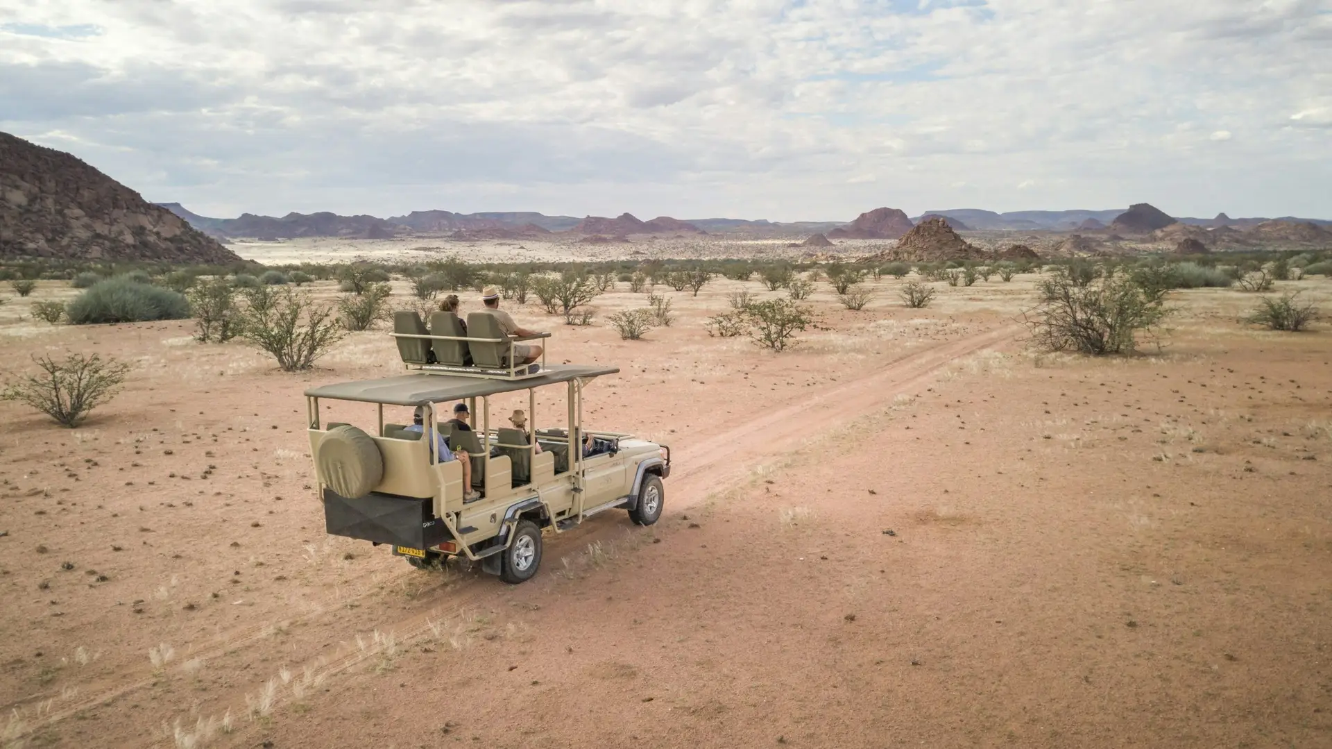 An Ultimate Safaris game vehicle with guide and guests tracking across the open plains of Damaraland, granite inselbergs on the horizon