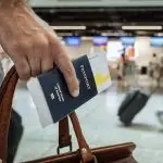 American traveler holding a US passport and boarding pass at an international airport, illustrating the new ETIAS travel authorisation requirement coming to Europe in late 2026