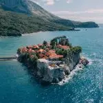 Aerial view of Sveti Stefan island, Montenegro, with the red-roofed restored medieval village and sand tombolo connecting it to the Adriatic coast.