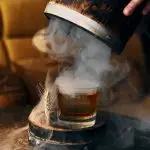 Best new bars 2026: a smoked whisky cocktail presented with a wooden cask and wheat garnish, capturing the technique-driven culture of the bars worth flying for in 2026