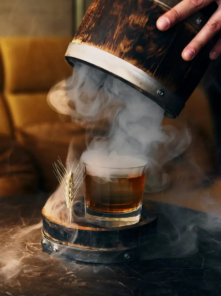 Best new bars 2026: a smoked whisky cocktail presented with a wooden cask and wheat garnish, capturing the technique-driven culture of the bars worth flying for in 2026