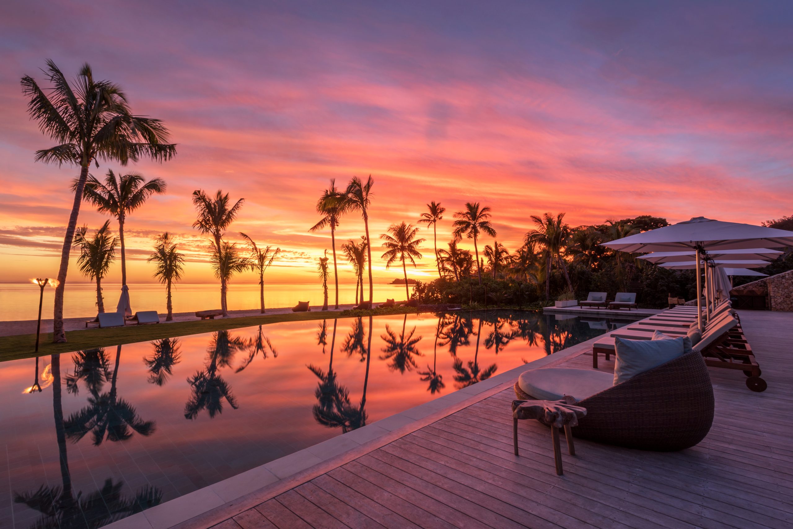 Six Senses Fiji Opens Three Beachfront Residences on Malolo Island 6 Sunset over the main infinity pool at Six Senses Fiji on Malolo Island, with palm silhouettes and pink sky reflecting in the water