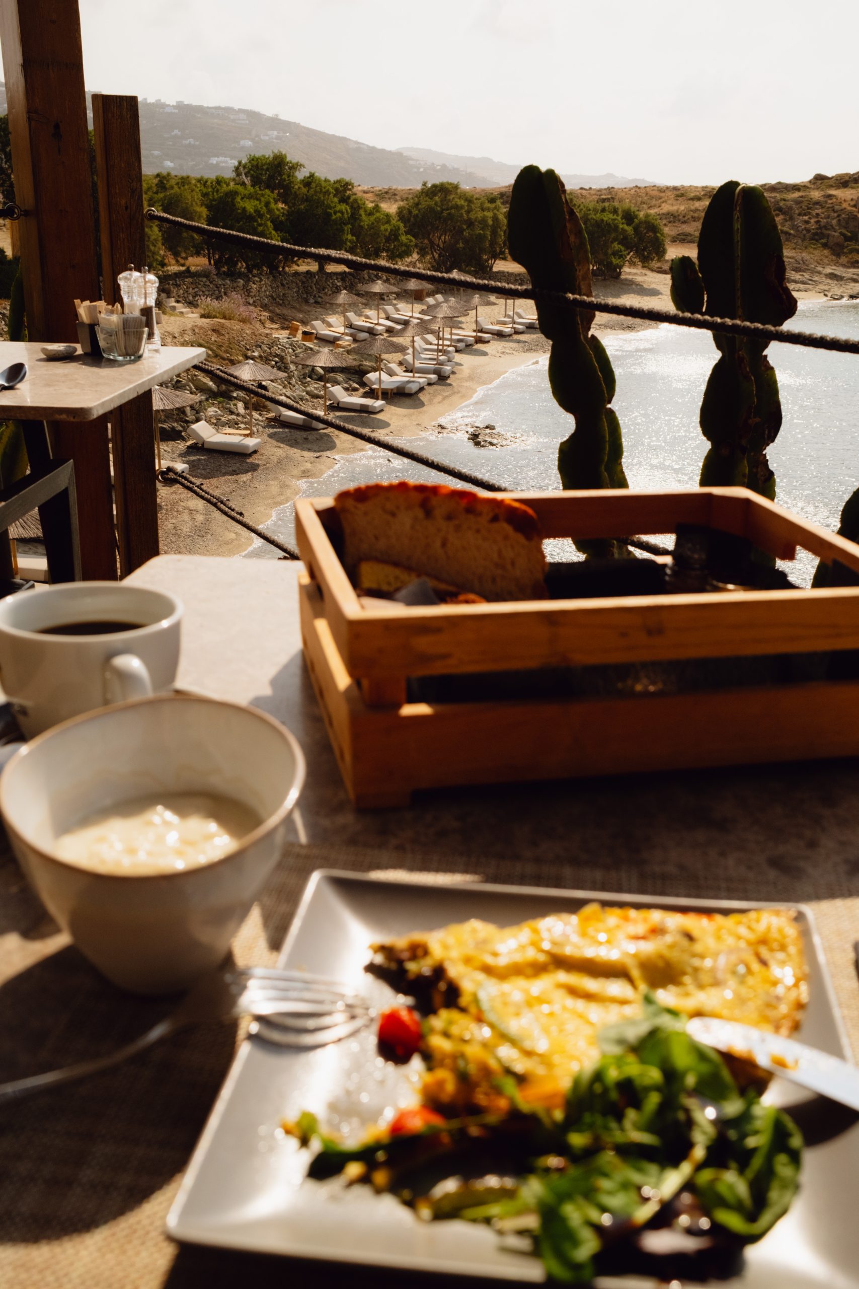 Casa Del Mar Mykonos: A Week on the Quiet Side of the Island 14 Breakfast on the terrace at Casa Del Mar Mykonos in the morning light, with an omelette, a basket of bread and coffee, overlooking Glyfadi cove and its sun loungers below