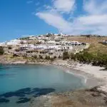 Casa Del Mar Mykonos review: the villas seen from across Glyfadi cove, whitewashed and stepping down the hillside above two rows of thatched umbrellas and sun loungers on the sandy beach
