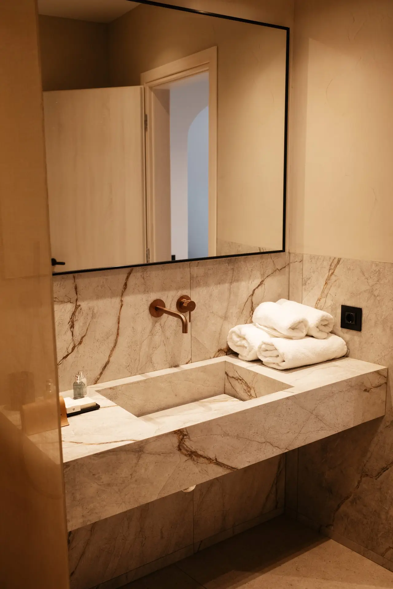 Casa Del Mar Mykonos: A Week on the Quiet Side of the Island 6 Marble bathroom in the Royal Beachfront villa at Casa Del Mar Mykonos, with a carved stone sink, wall-mounted copper tap, large mirror, and rolled white towels