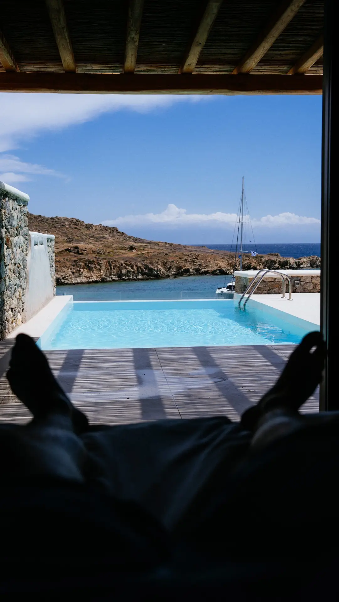 Casa Del Mar Mykonos: A Week on the Quiet Side of the Island 18 View from the bed in the Royal Beachfront villa at Casa Del Mar Mykonos, looking past the private infinity pool to the cove and a sailboat on the blue Aegean