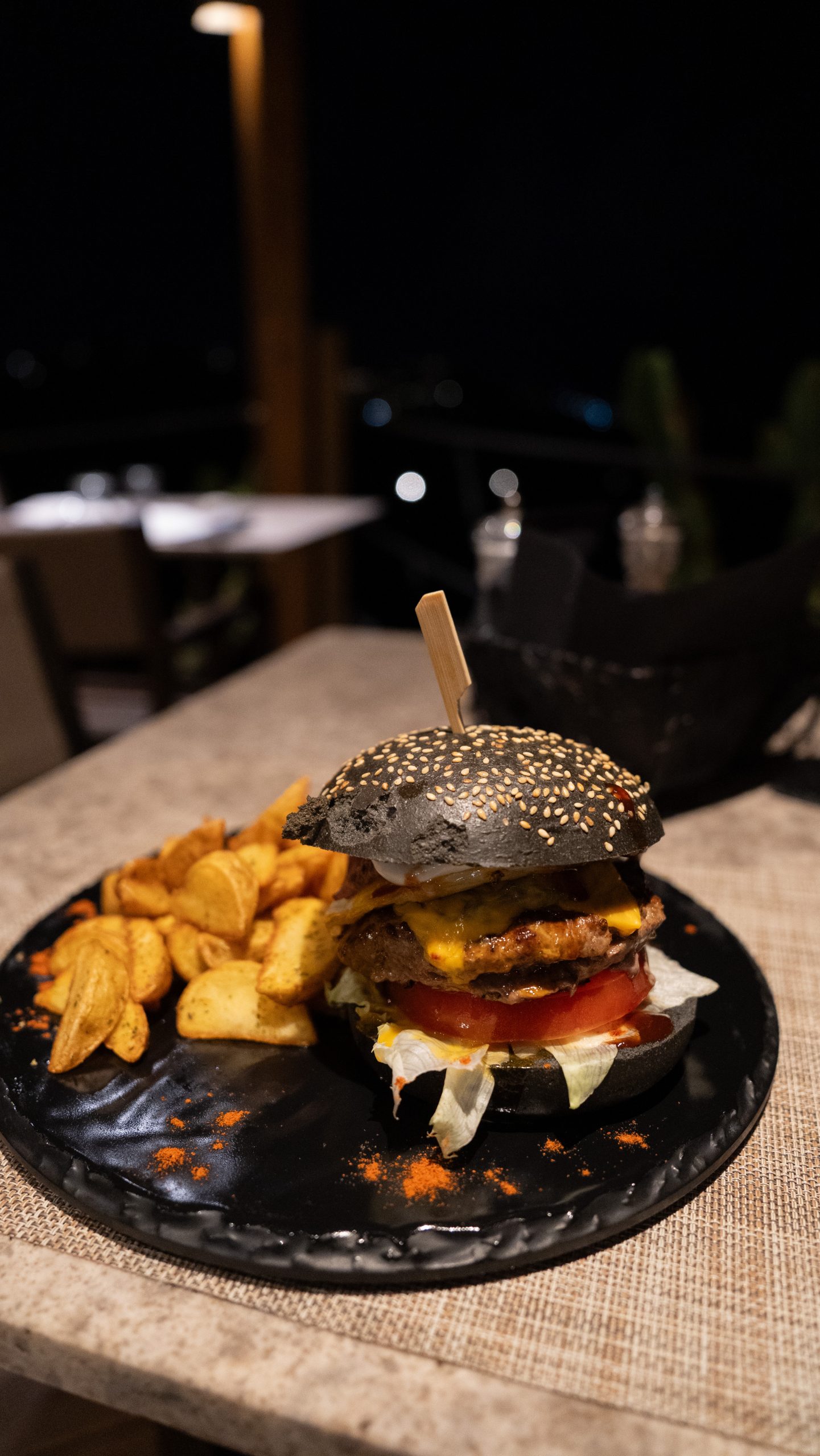 Casa Del Mar Mykonos: A Week on the Quiet Side of the Island 12 Casa beef burger on a jet-black charcoal sesame bun with melted cheddar, tomato and lettuce, served with potato wedges on a dark plate at Miramar restaurant, Casa Del Mar Mykonos