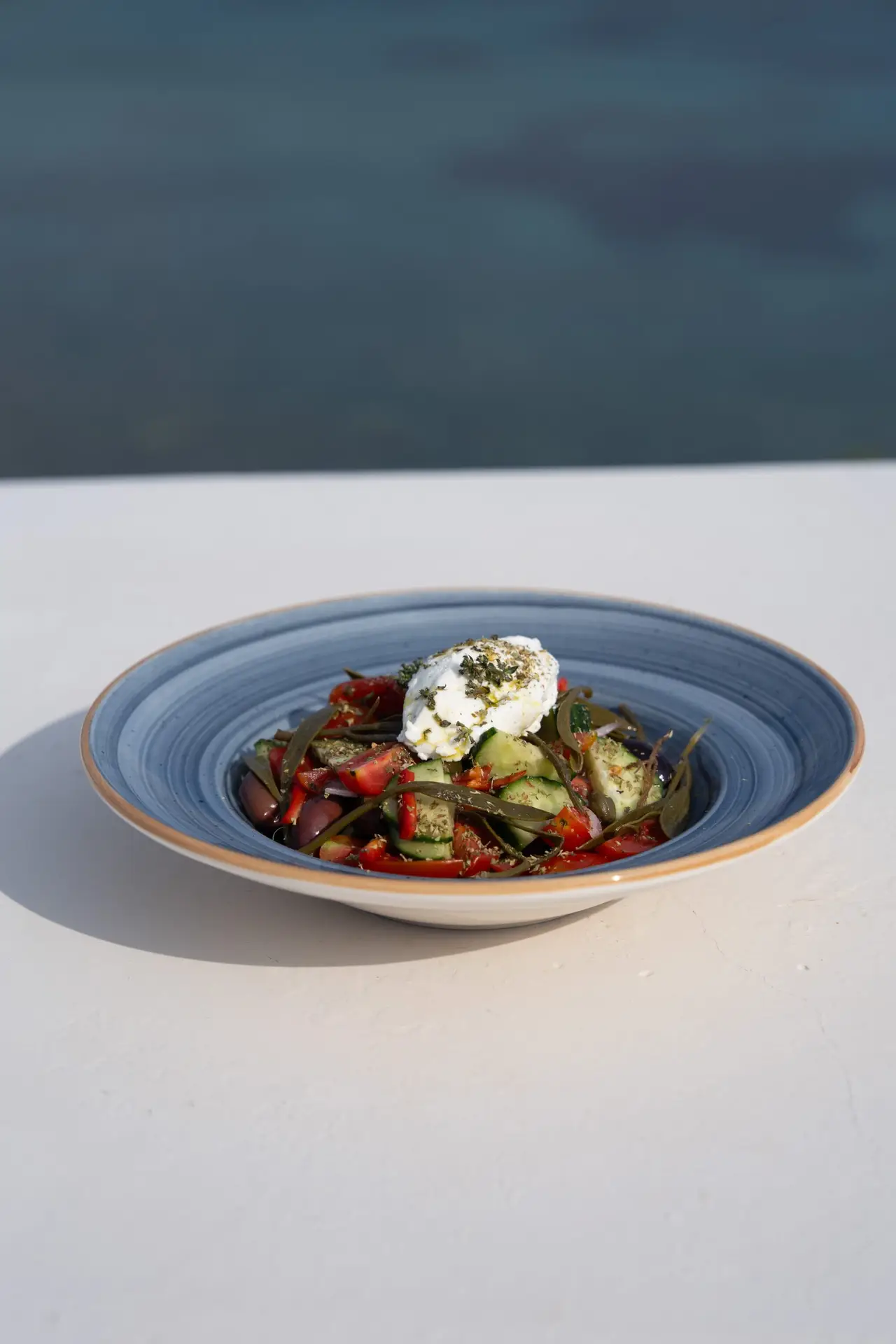Casa Del Mar Mykonos: A Week on the Quiet Side of the Island 13 Signature Greek salad with tomatoes, cucumber, kalamata olives and a creamy feta topping dusted with oregano, in a blue ceramic bowl against the sea at Miramar restaurant, Casa Del Mar Mykonos