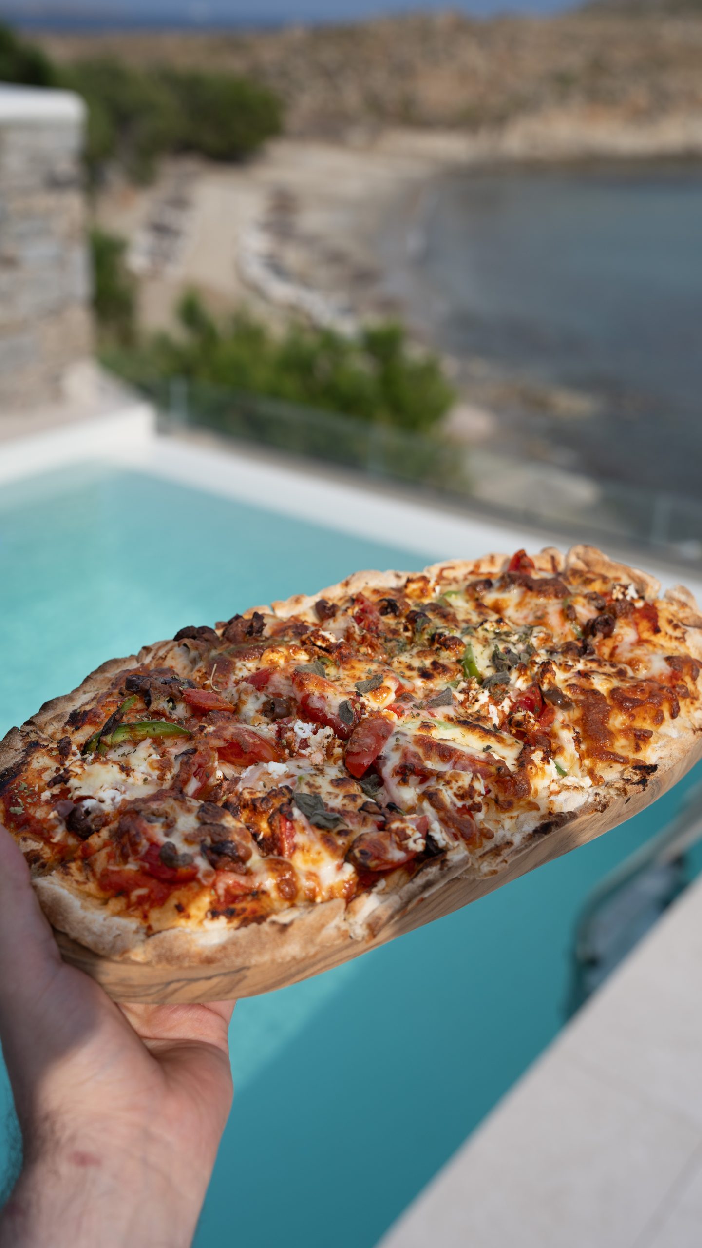 Casa Del Mar Mykonos: A Week on the Quiet Side of the Island 11 Pinsa greca on a wooden board held up in front of the private pool and Glyfadi cove at Casa Del Mar Mykonos, topped with tomatoes, feta, olives, peppers and oregano