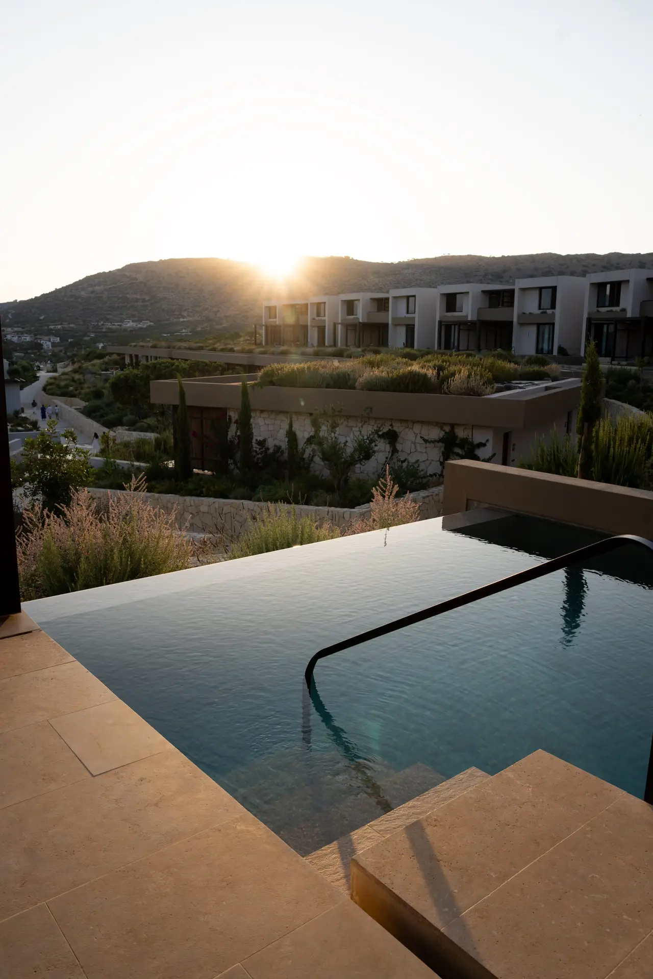 Sunset view from a Deluxe Suite pool at JW Marriott Crete, over planted roofs and terraced suites on the hillside