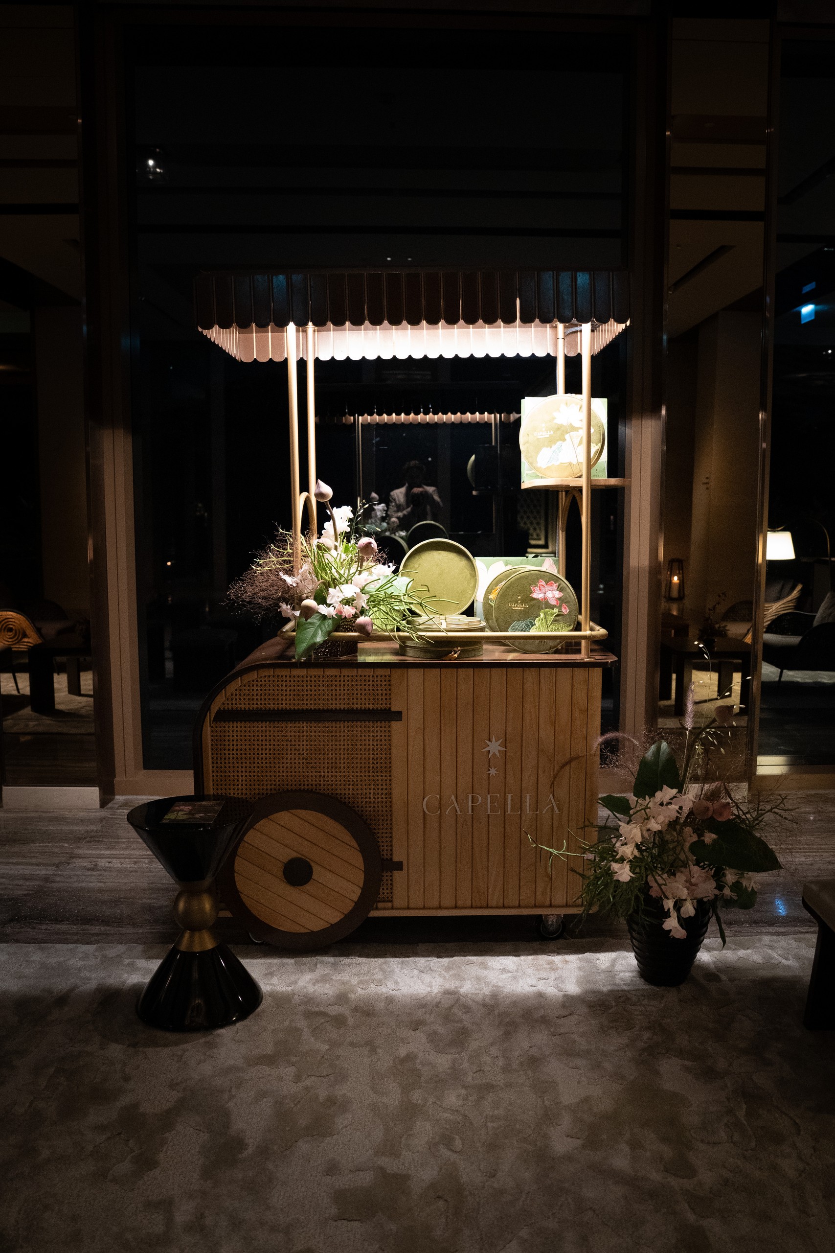 Wooden Capella cart with flowers and gold tins at night at Capella Bangkok