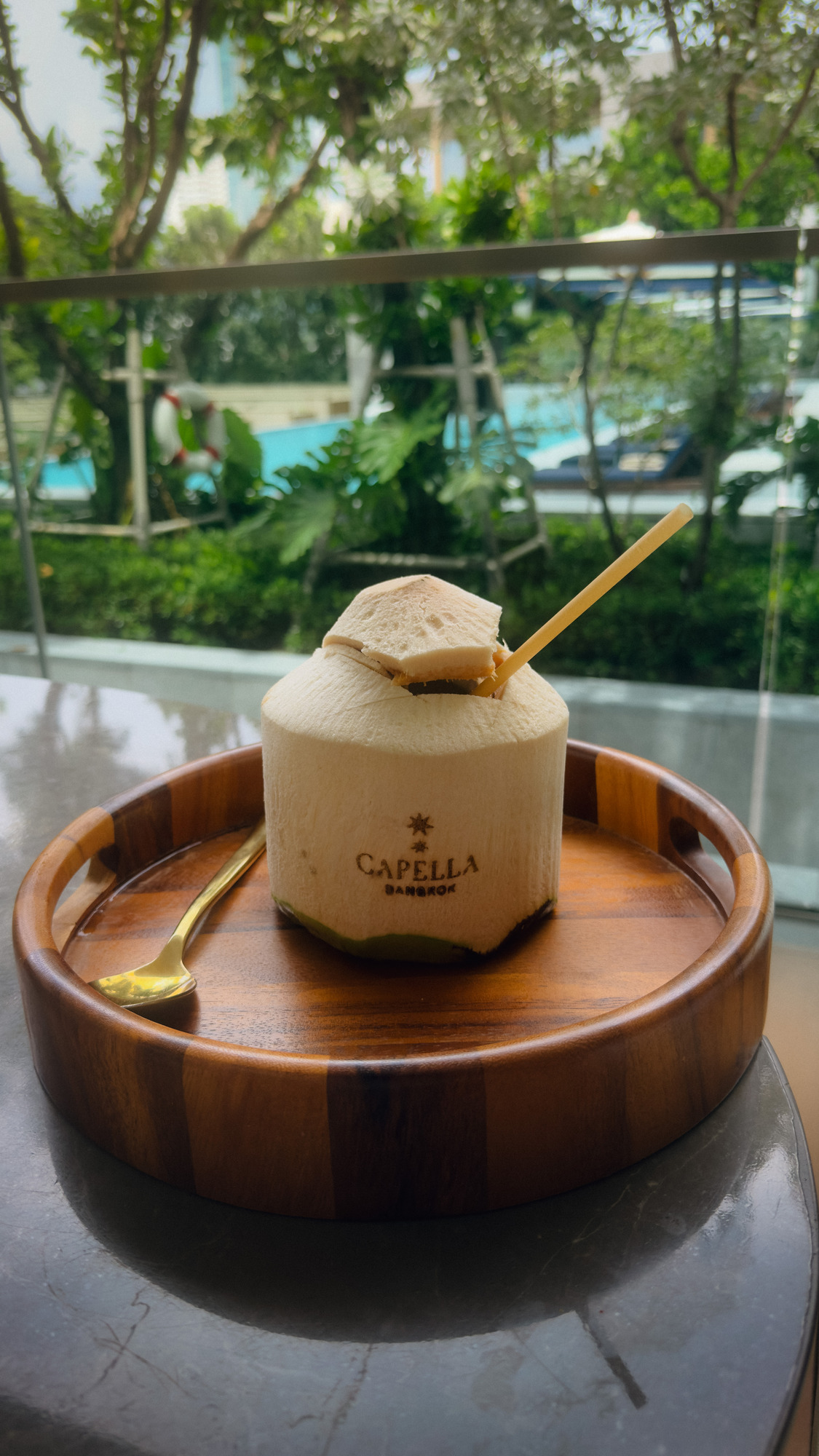 Fresh coconut with the Capella logo on a wooden tray by the pool at Capella Bangkok