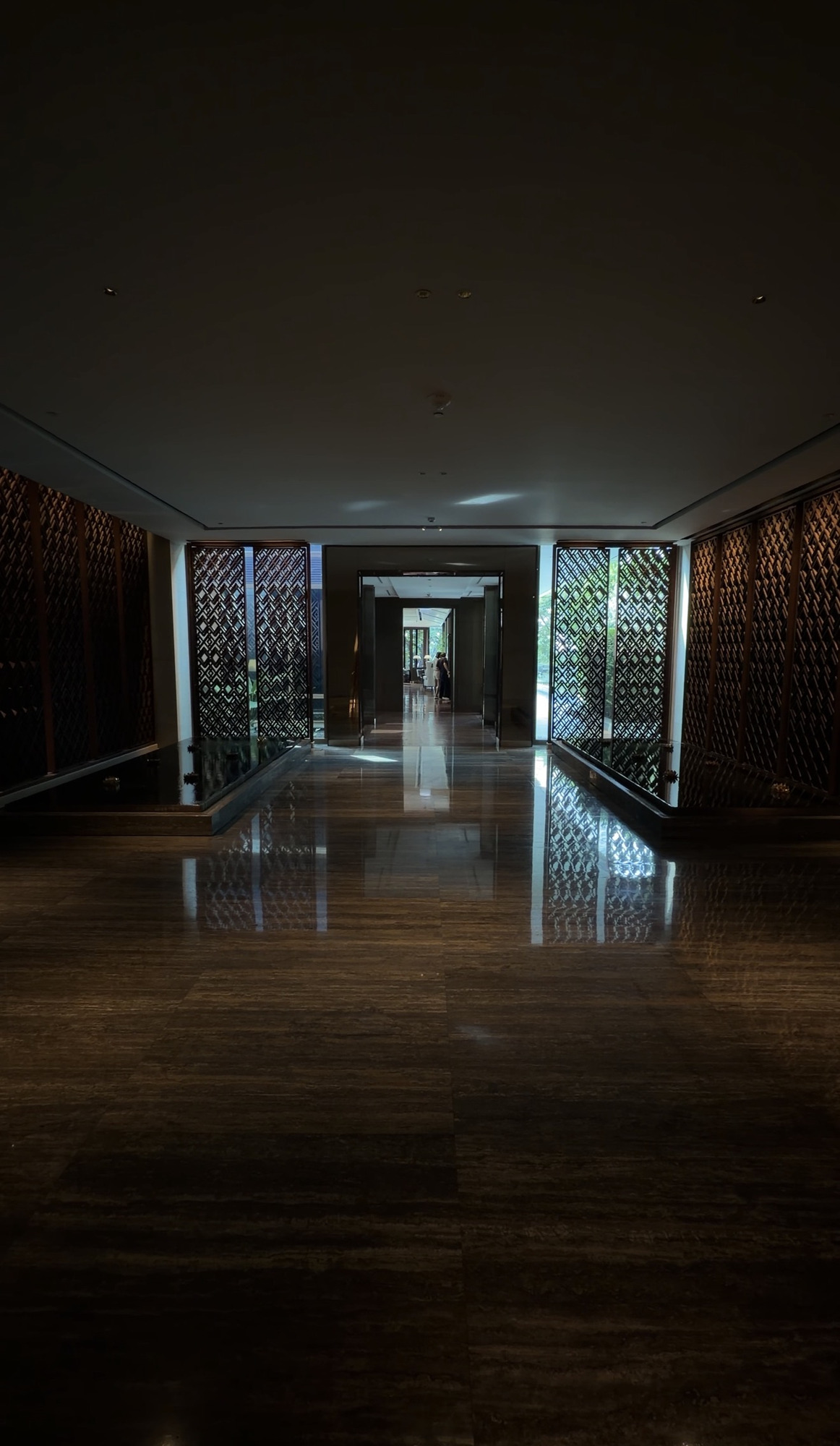 Dark corridor with wooden lattice screens leading to The Living Room at Capella Bangkok