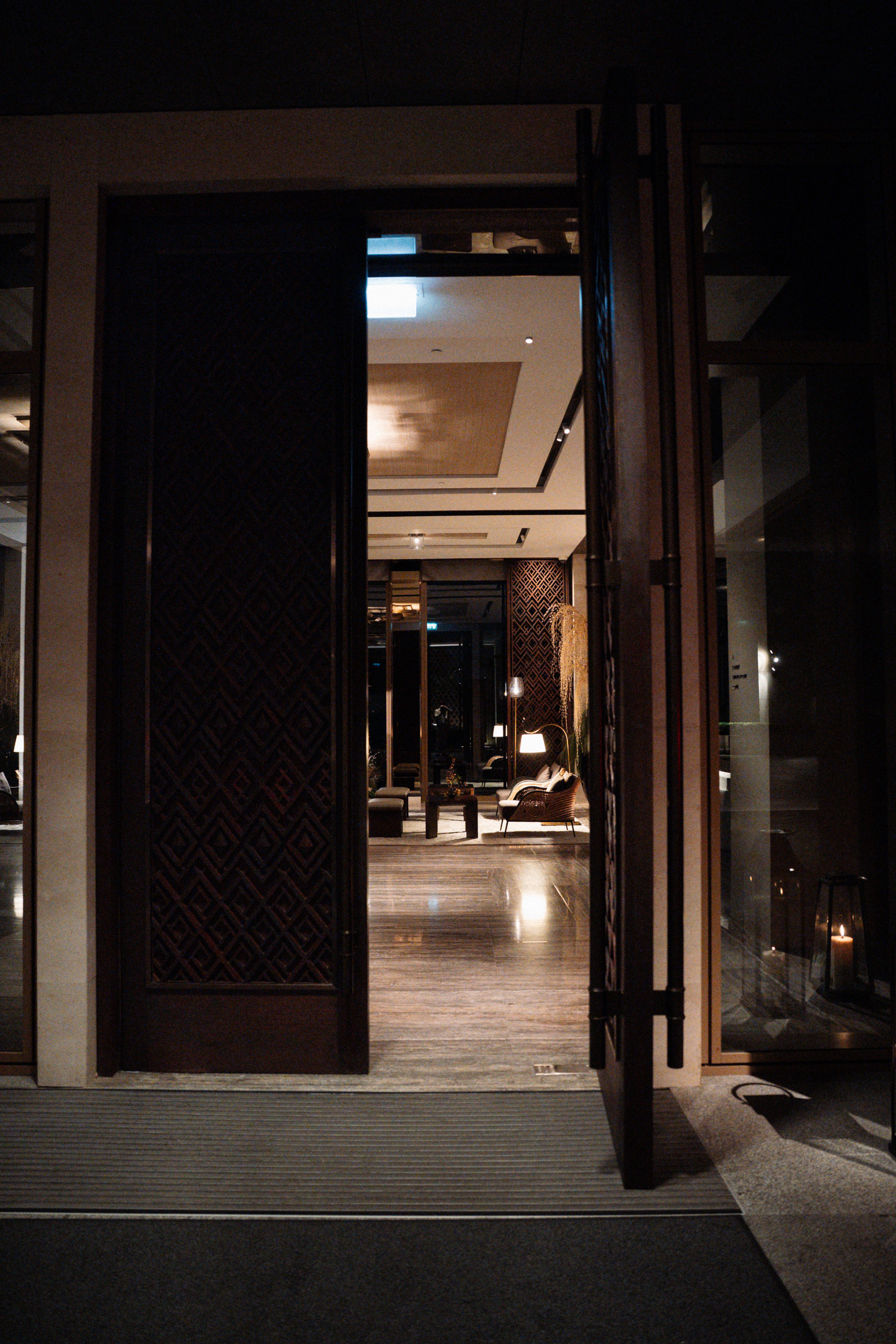 Open wooden entrance doors leading into the Capella Bangkok lobby at night