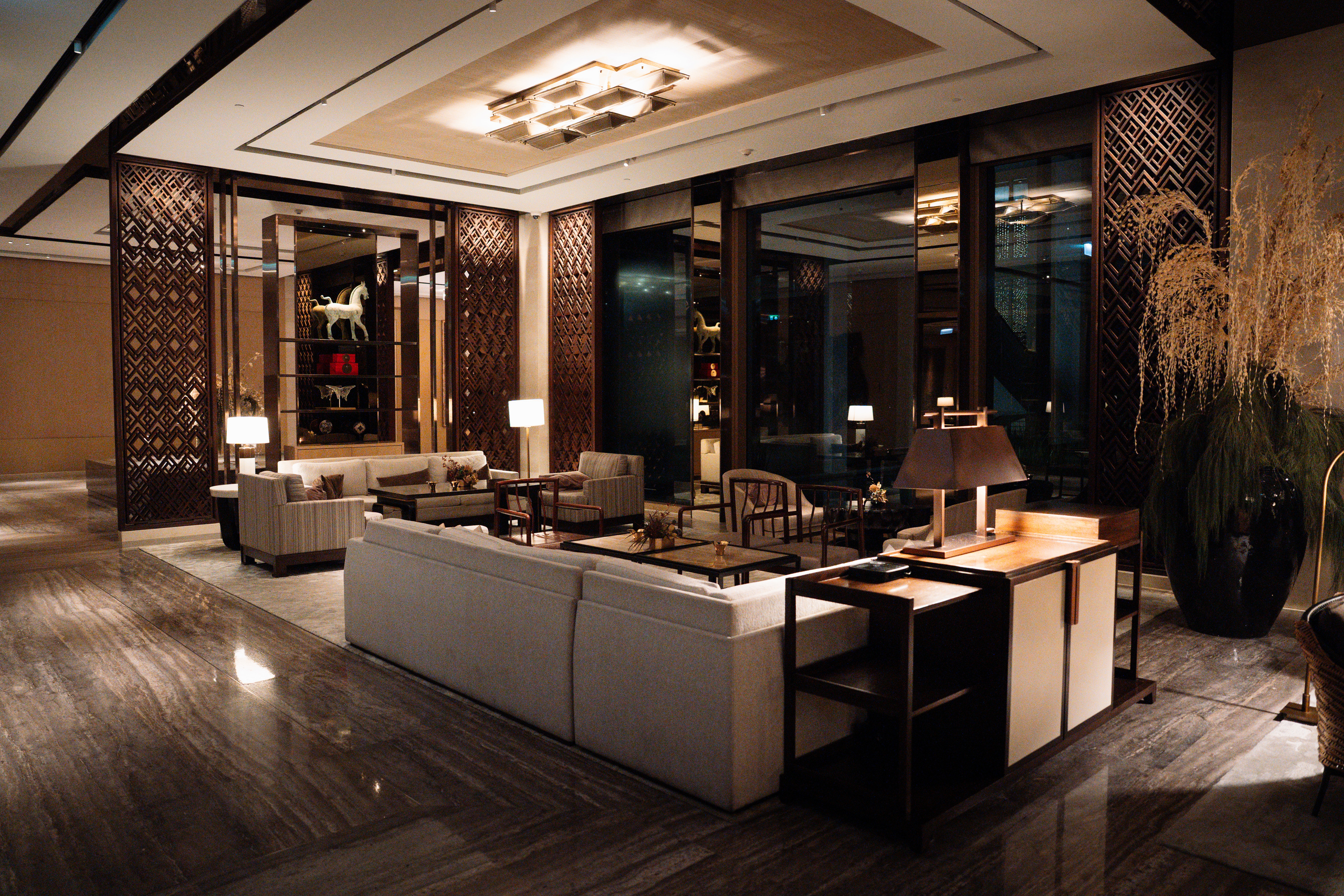 Sofas, lattice screens and warm lamps in the lobby at Capella Bangkok in the evening