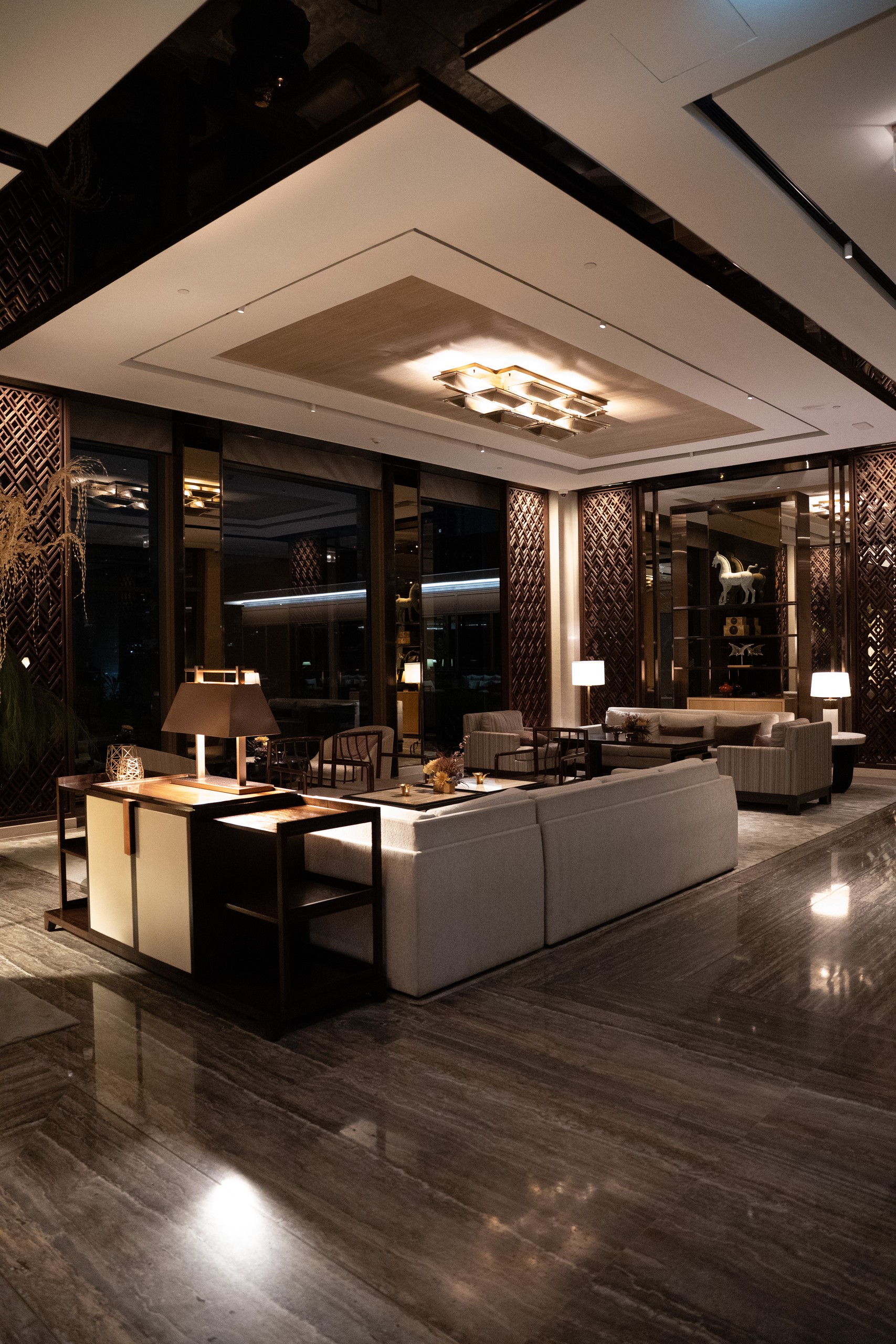 Lobby lounge with sofas, lattice screens and marble floor at night at Capella Bangkok
