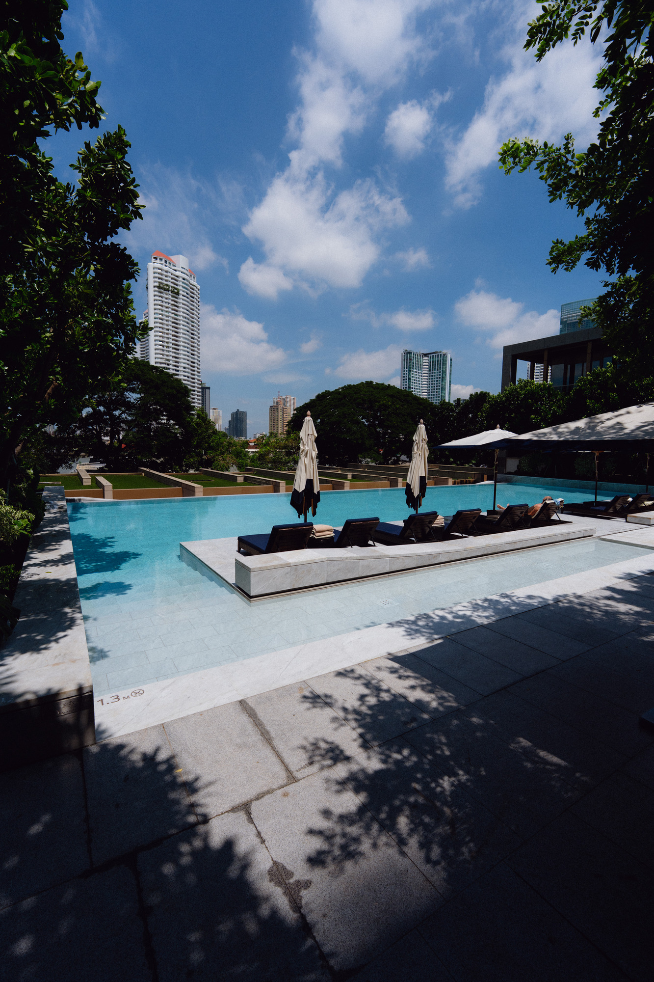 The pool in the garden at Capella Bangkok with loungers and trees