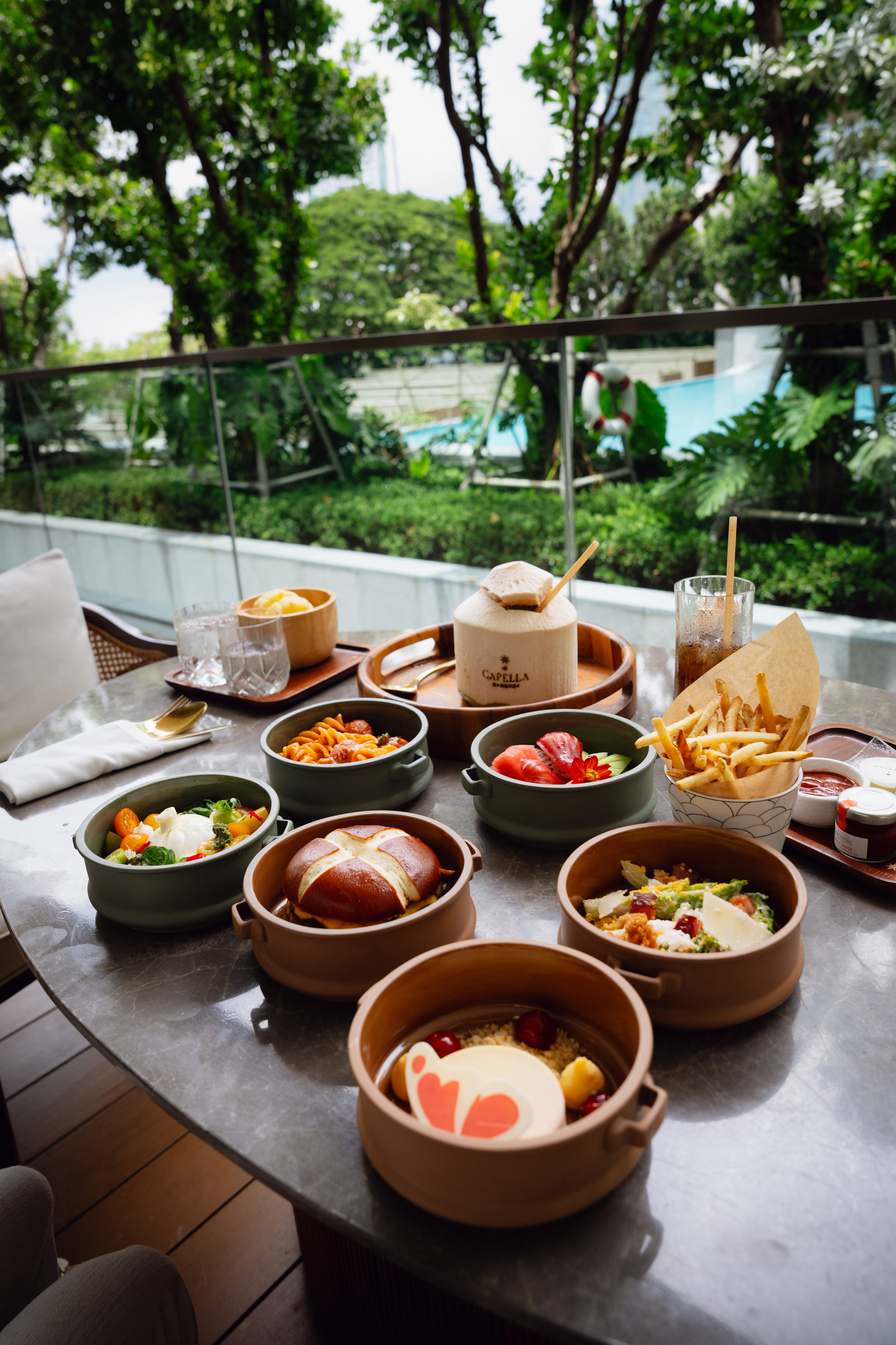 Lunch dishes spread across a table by the pool at Capella Bangkok