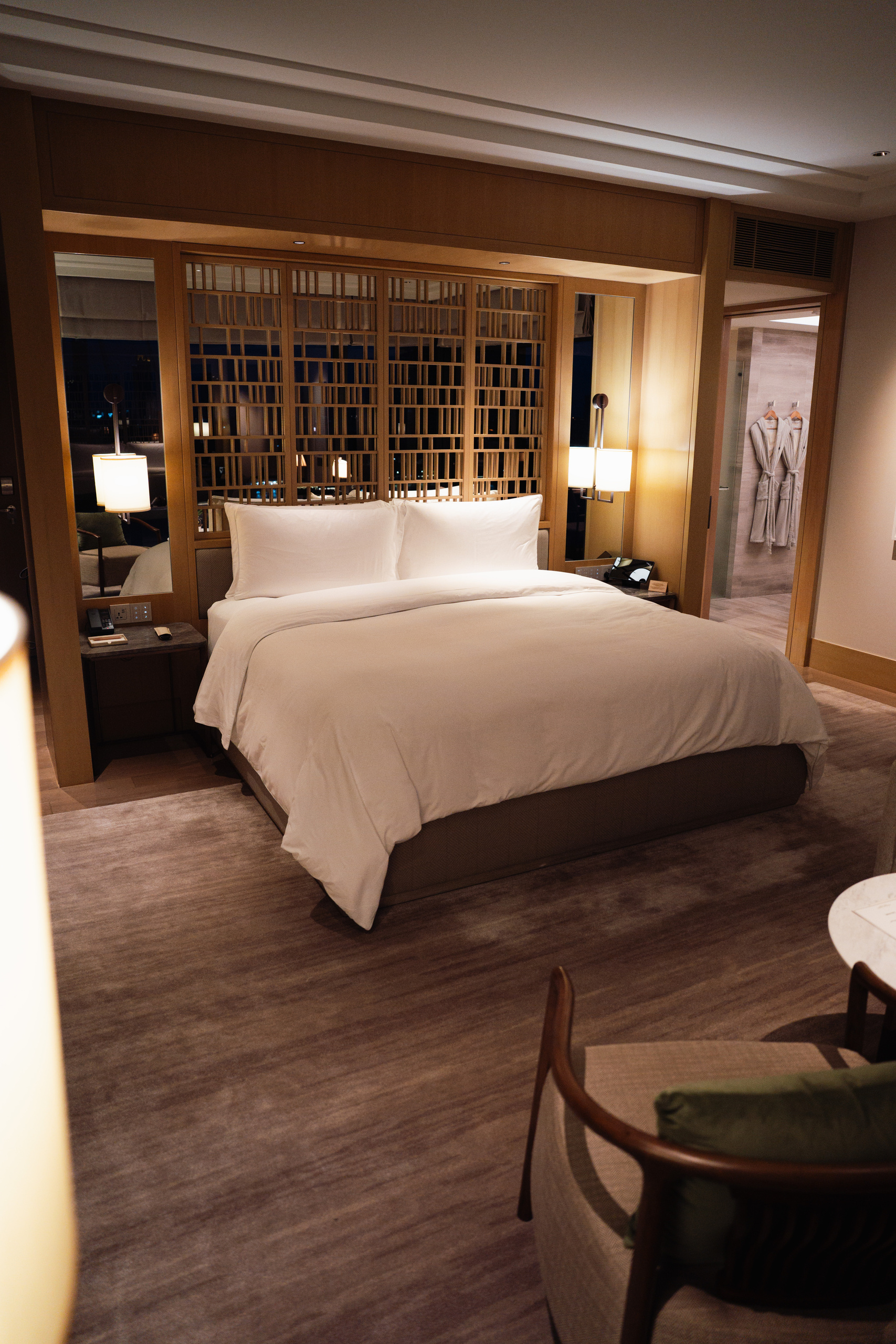 King bed with a lattice headboard in the Riverfront Premier room at Capella Bangkok in the evening
