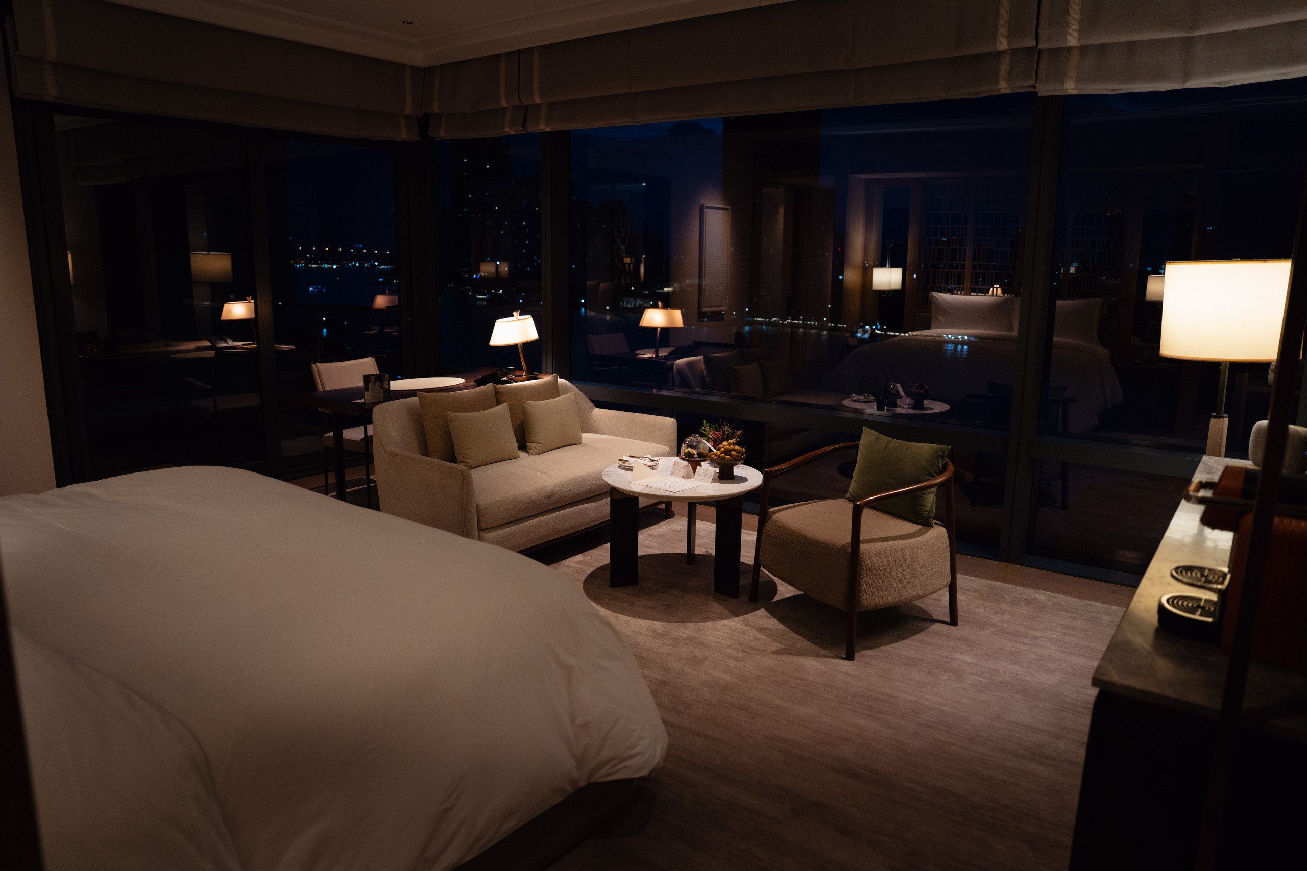 Riverfront Premier room at night with lamps lit and the river lights outside at Capella Bangkok
