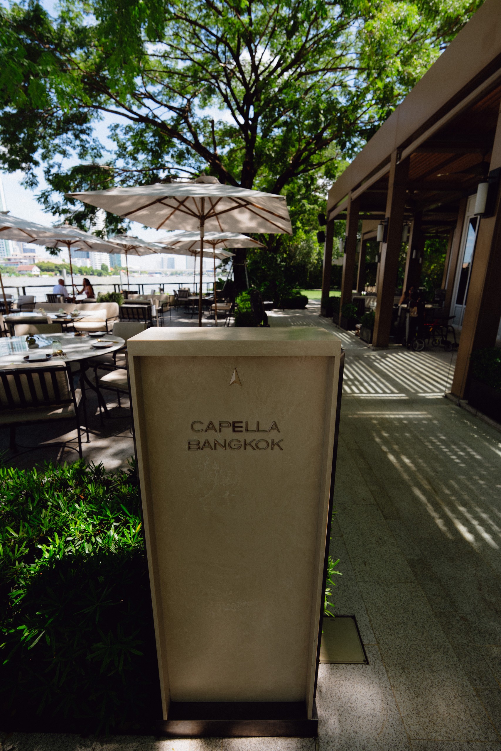 Capella Bangkok sign by the shaded riverside terrace with umbrellas
