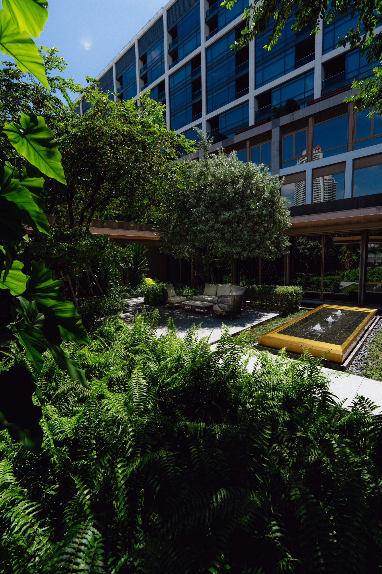Green garden with ferns, a fountain and seating outside the spa at Capella Bangkok