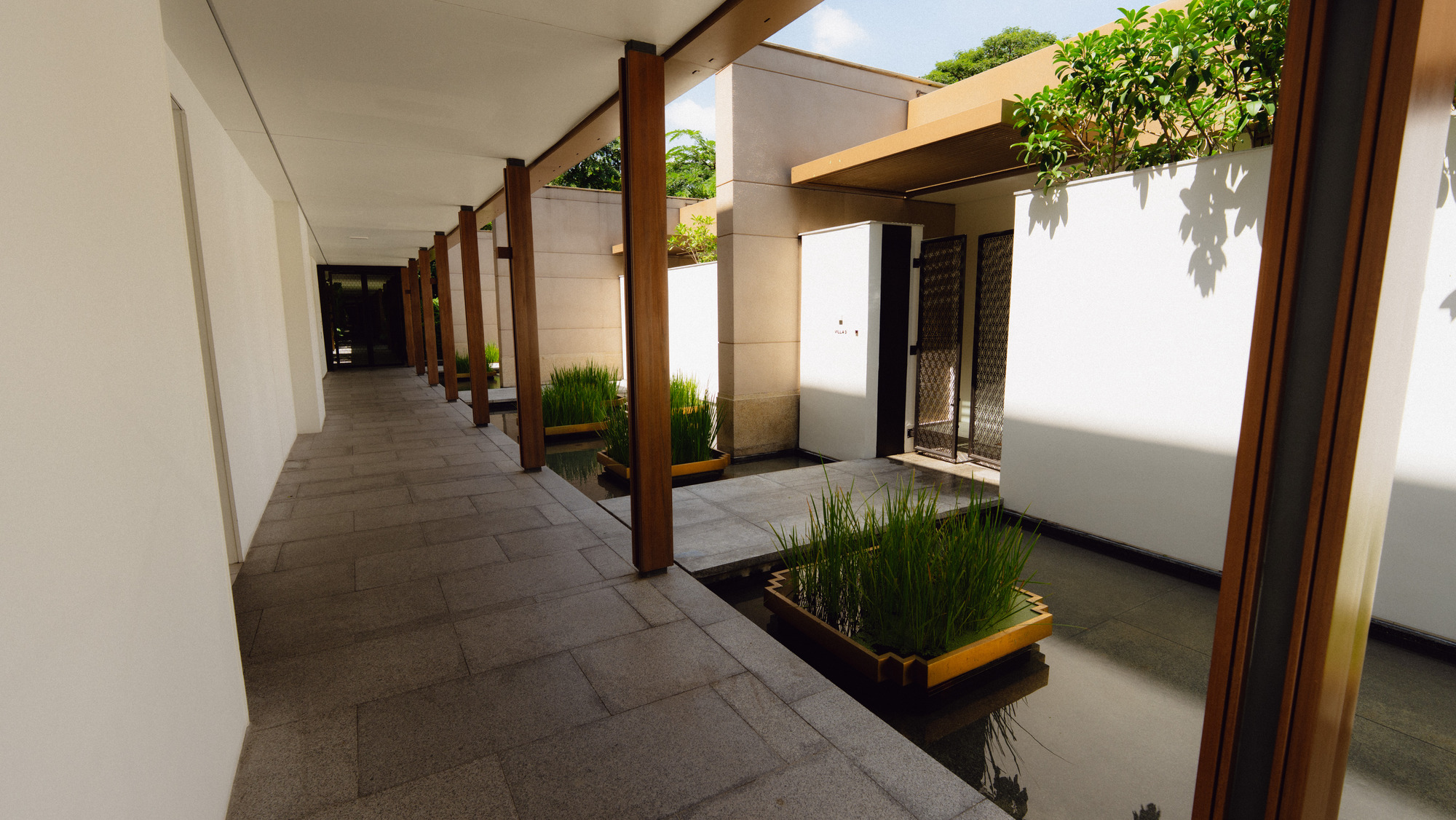 Walkway with columns and a reflecting pool past the villas at Capella Bangkok